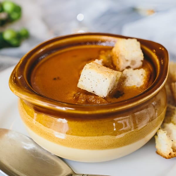 Rich brown Spanish soup in a two-toned ceramic bowl, topped with crunchy croutons.