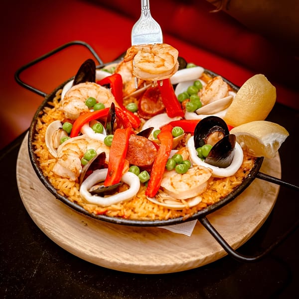 A fork lifts a shrimp from a Tio Pepe paella with seafood, chorizo, peppers, and peas.