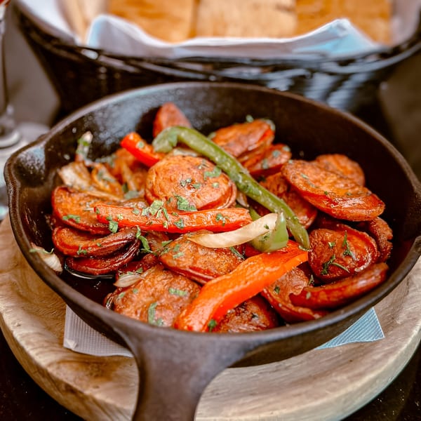 Sizzling Spanish chorizo sausage with red and green peppers, garnished with parsley in a cast iron pan.