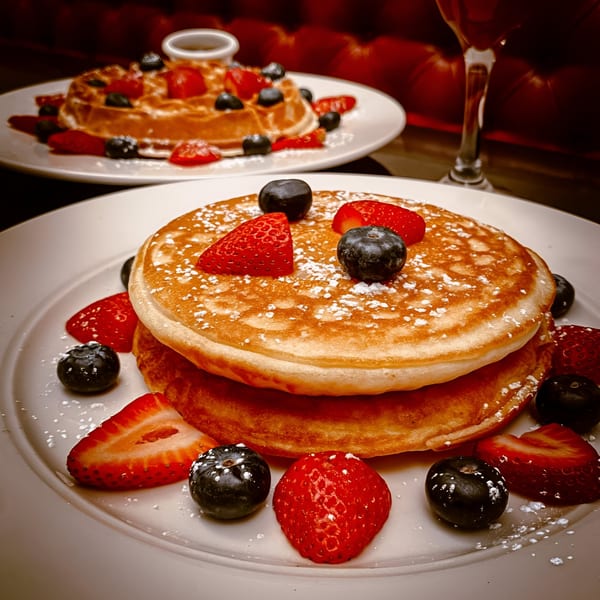 Fluffy pancakes and a waffle, both topped with fresh strawberries, blueberries, and powdered sugar.
